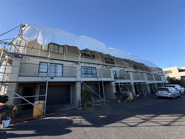 Residential exterior renovation in progress with scaffolding and protective sheeting